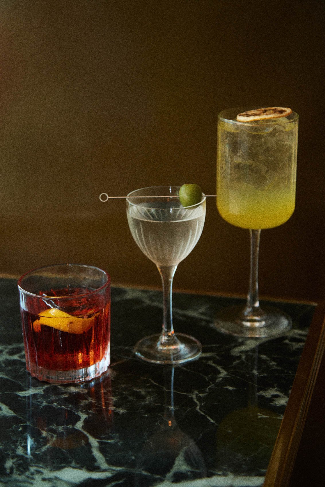 Three cocktails lined up on the marble bar top at Bar Premio