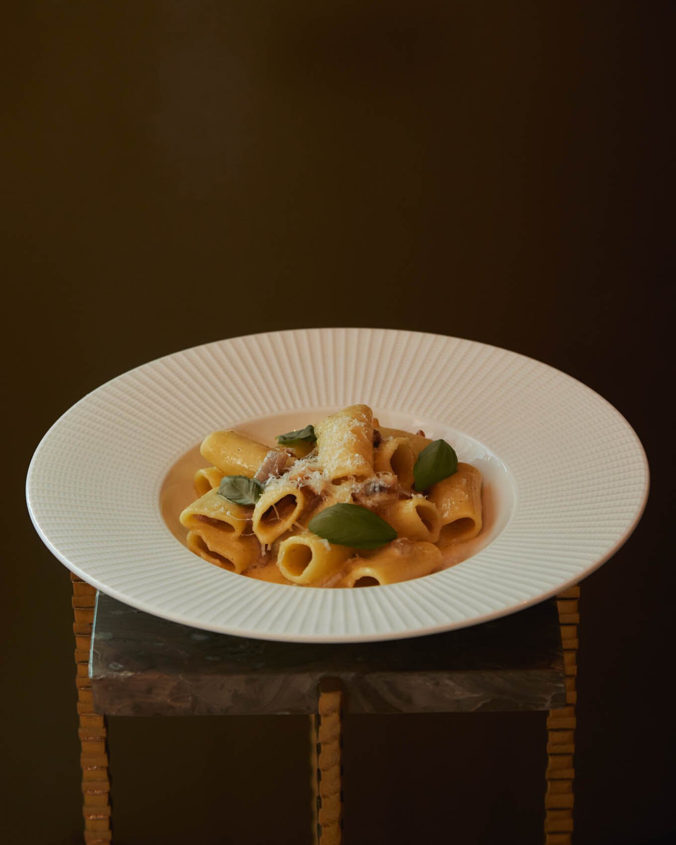 A bowl of rigatoni finished with basil, on a marble pedestal