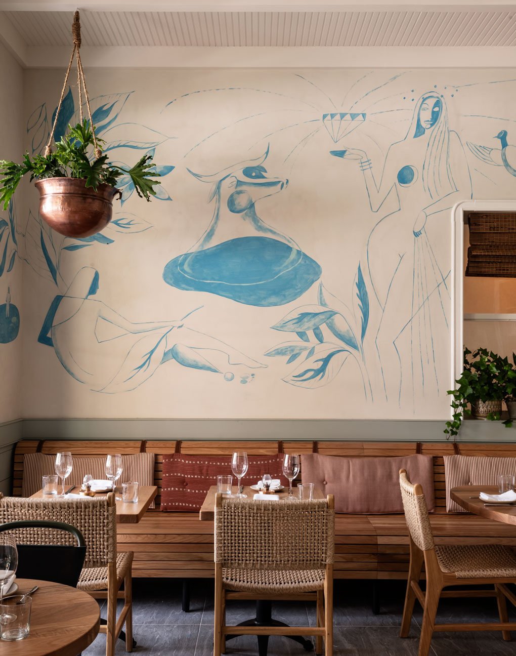 A hanging planter in front of Elektra’s blue figurative mural above the banquette